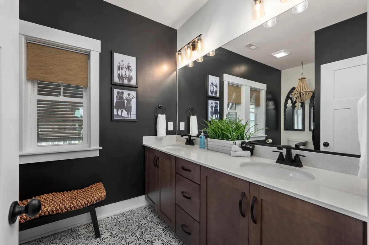 A contemporary ensuite bathroom with a dark accent wall, dual-sink vanity, decorative lighting, and framed wall art. Green plant accents and soft lighting create a calming and spa-like ambiance, ideal for moments of relaxation and self-care.