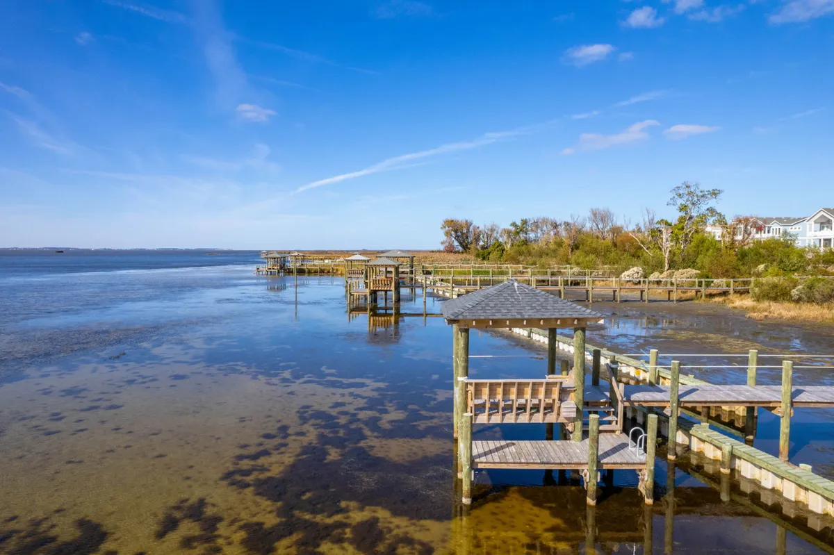 A serene view of wooden docks stretching out over calm water, lined with green foliage and a blue sky above. The dock is perfect for fishing, paddleboarding, or quiet reflection.