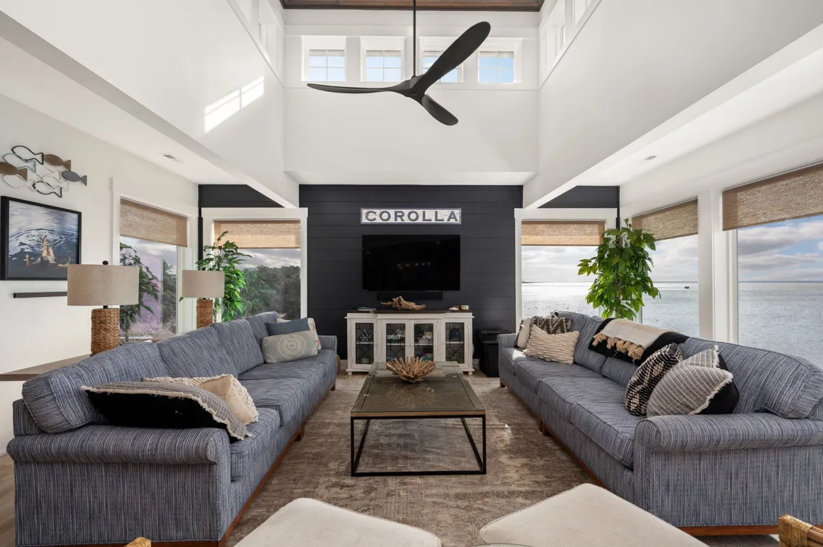 An inviting living space with two large sofas facing each other, a wall-mounted television, a stylish coffee table with decorative centerpiece, and expansive windows offering tranquil water views. This room exudes relaxation and is perfect for movie nights or board games.