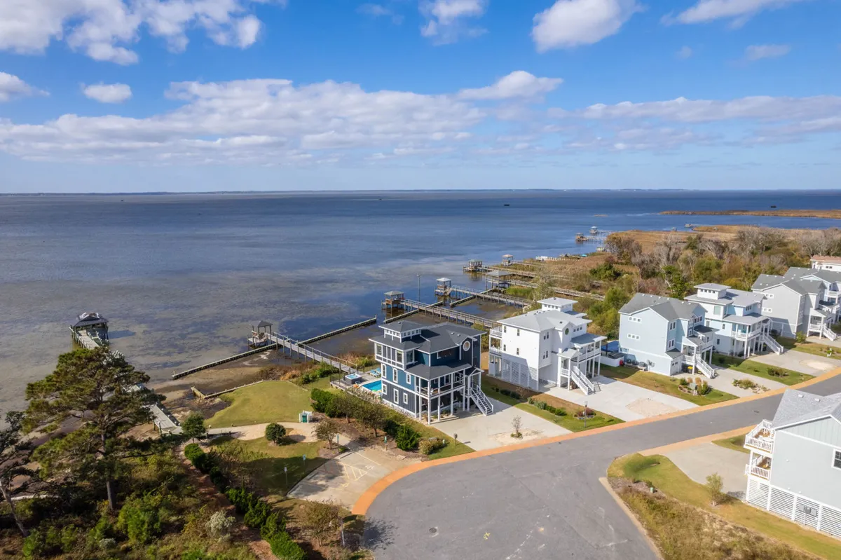 A wide view of the water with several docks and nearby houses nestled among trees, suggesting a tranquil neighborhood atmosphere. The open water and natural setting make it ideal for kayaking, paddleboarding, and birdwatching.