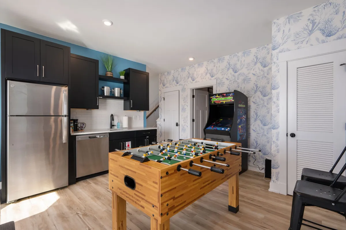 A lively interior shot of a game room with a foosball table, arcade game machine, modern kitchen appliances, and cheerful decor. The atmosphere is energetic and playful, inviting group activities and friendly competition.