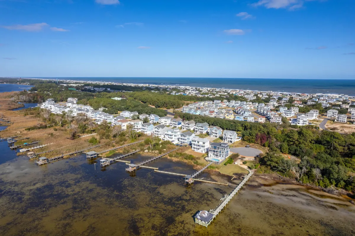 A wide view of the neighborhood: waterfront properties nestled against marshland and open ocean, with docks stretching into the water. The scene exudes natural beauty and hints at wildlife and seasonal changes.