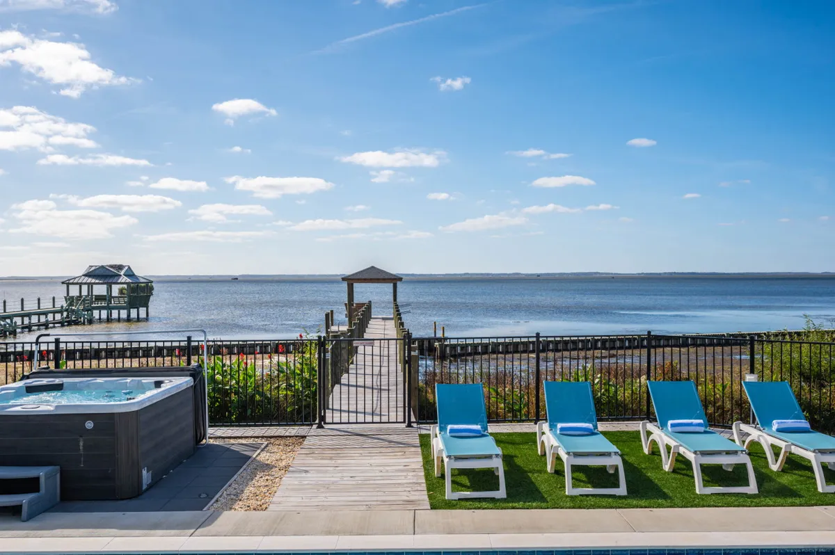 A private dock extends over calm water, featuring a hot tub, lounge chairs, and open sky. The scene evokes relaxation, outdoor leisure, and soaking in picturesque sunsets—activities synonymous with a Corolla vacation.