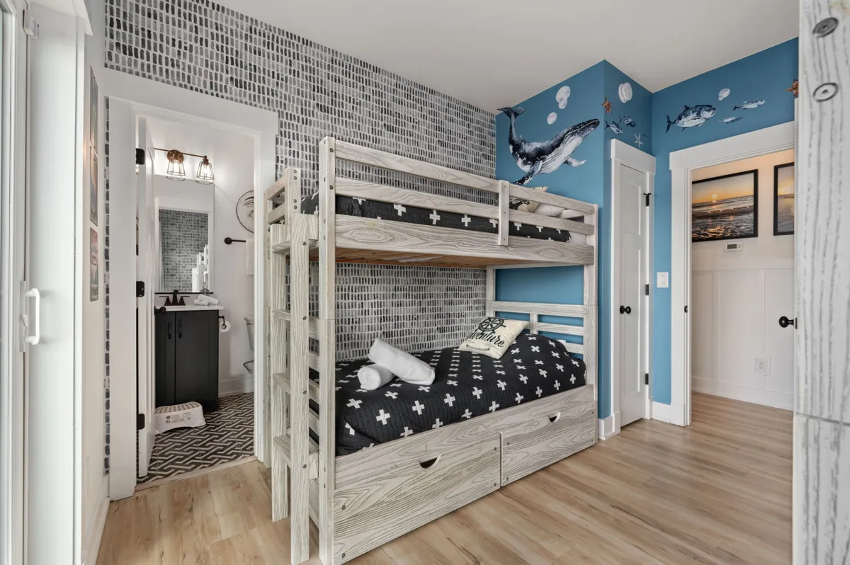 This playful bunk room features a bunk bed with a fun shark mural and a black-and-white patterned rug. The setup is colorful and whimsical, creating a space perfect for children, sleepovers, or family story time.